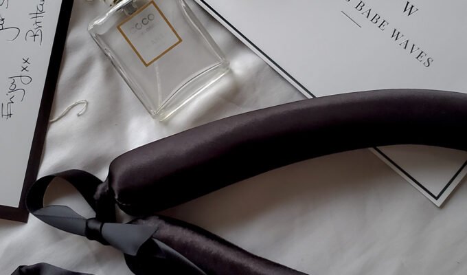 Black satin heatless curling ribbon, scrunchies, pearl hair clip and perfume arranged on a white bed