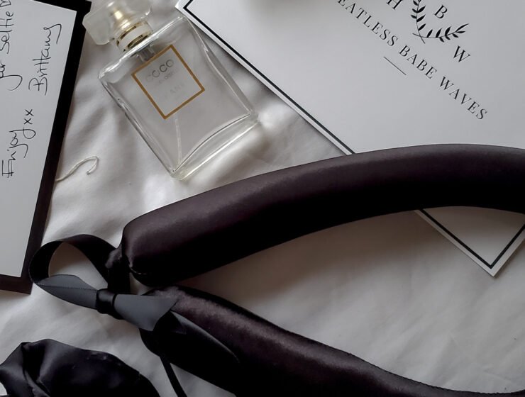 Black satin heatless curling ribbon, scrunchies, pearl hair clip and perfume arranged on a white bed